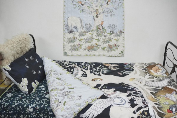 Close up of Forivor's Enchanted Forest Bedding shown with the Enchanted Forest Quilted Blanket hanging on the wall and the Hidden Foxes and Tumbling Pegasus Blanket on the Bed.