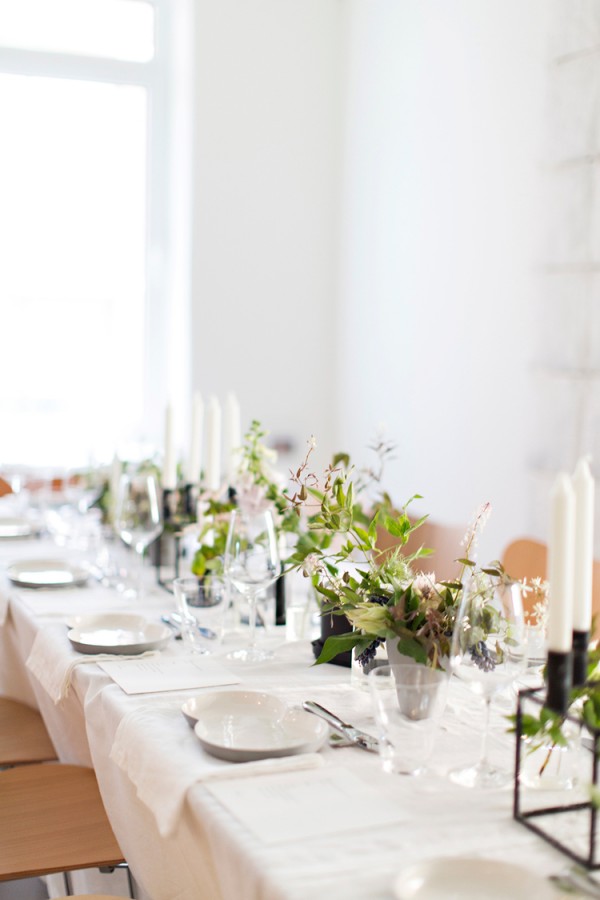 Create a Nordic-themed tablescape by keeping things clean and simple. Sunday Suppers used white linens, minimalist ceramics and glassware from the VIPP line. "A combination of simple greens and white flowers were used in both small bud vases on the table and in large arrangements throughout the loft, created by Anna of Fox Fodder Farms."